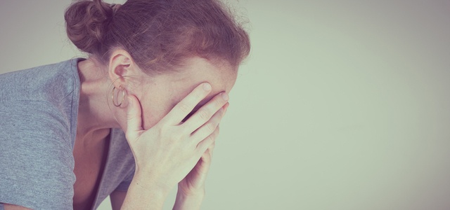 one sad woman sitting near a wall and holding her head in her hands