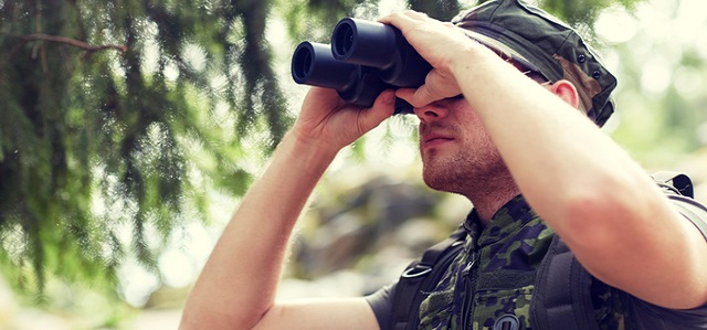 hunting, war, army and people concept - young soldier, ranger or hunter with binocular observing forest