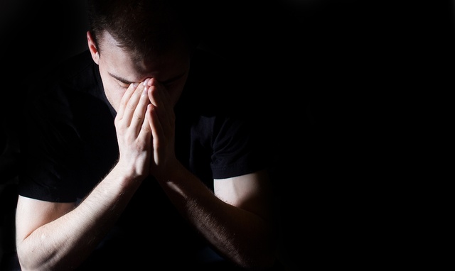 Low-key portrait of stressed young man with hands on a face, lonely, sad, negative